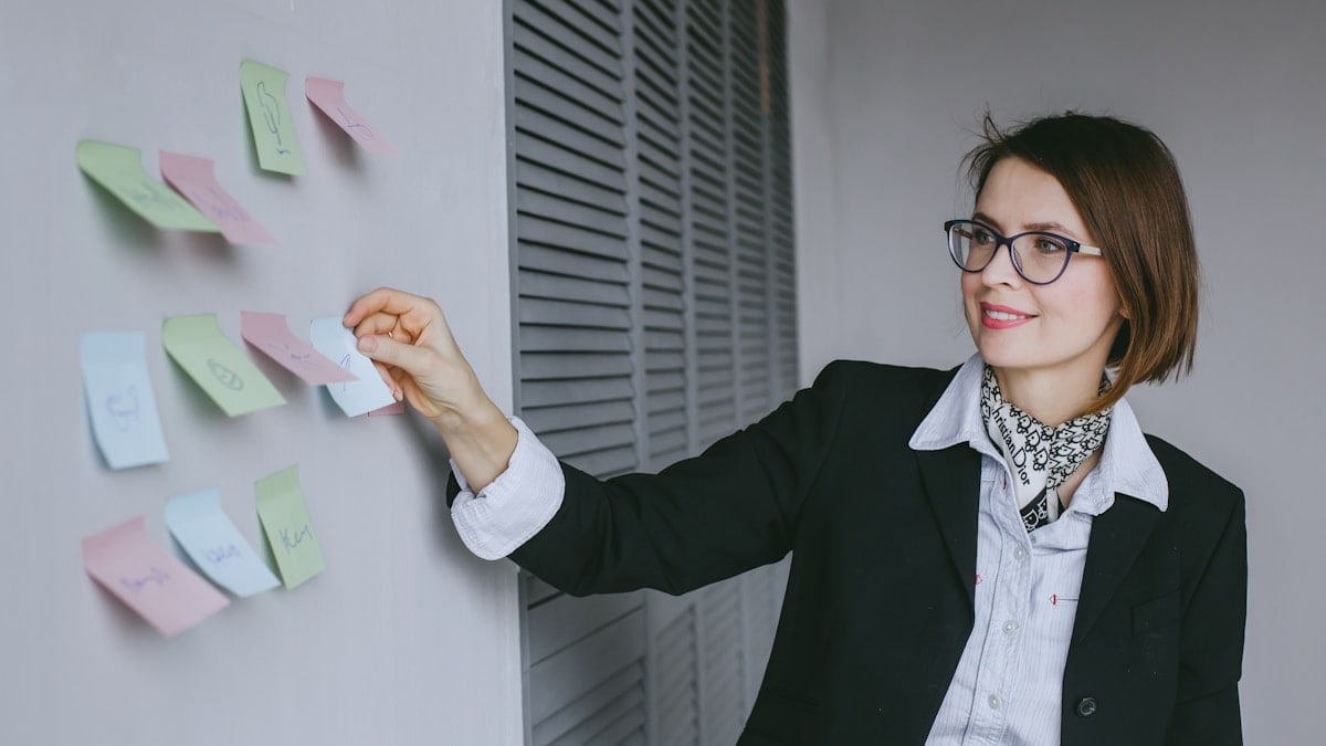 a woman in a black jacket and glasses writing on a wall